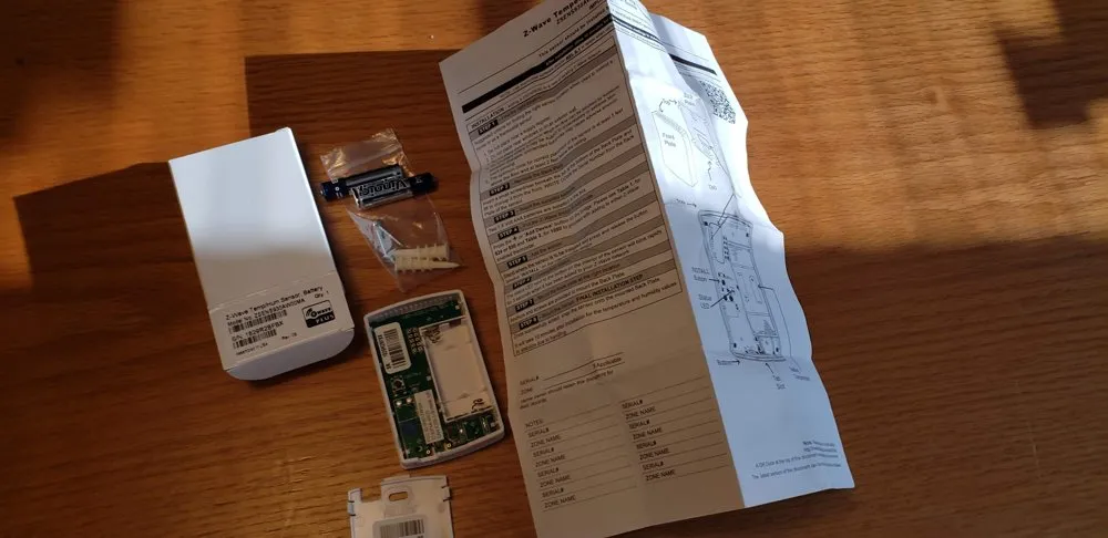 Wireless sensor hardware laid out next to its folded instruction sheet
